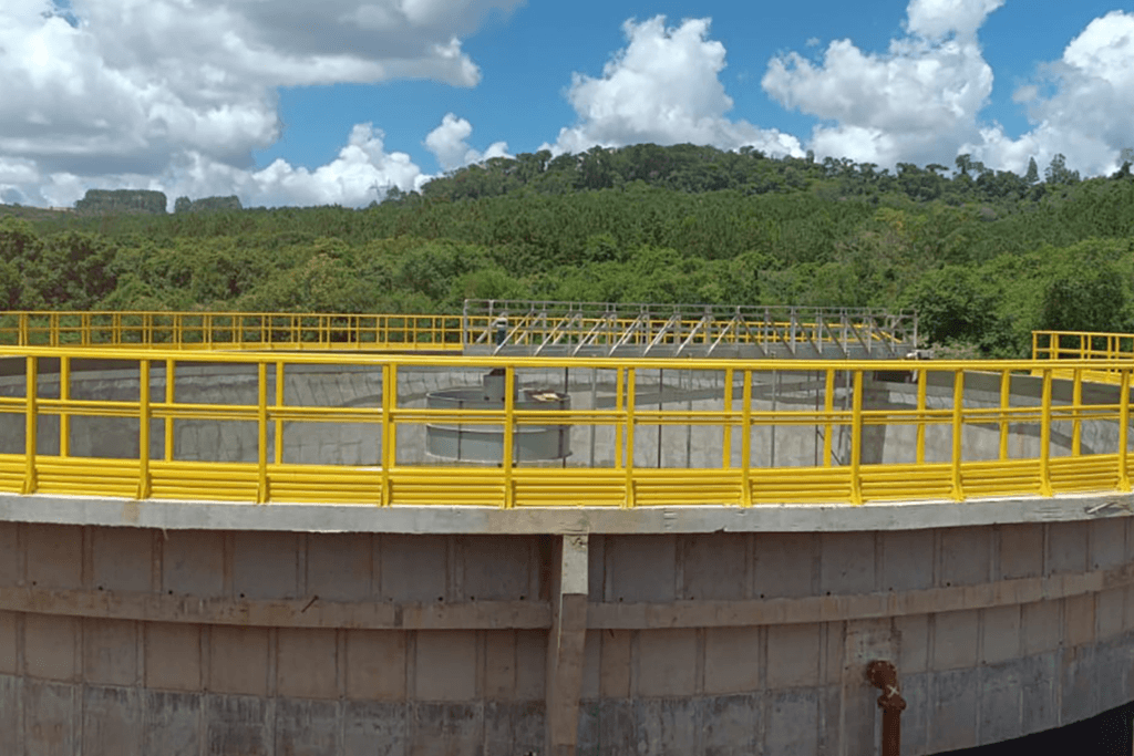 Estrutura circular em concreto com guarda-corpos amarelos instalada em ambiente de saneamento, evidenciando uma solução voltada à segurança operacional, resistência e durabilidade em área externa. A imagem destaca a aplicação da estrutura em um contexto técnico, com integração à operação e adaptação às exigências do projeto.